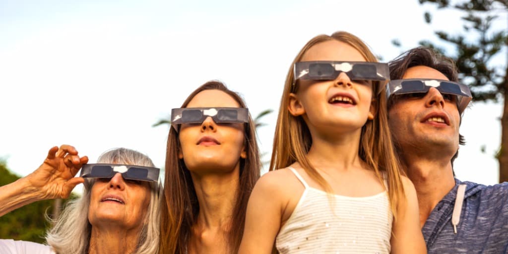 Photo d'une famille se protégeant lors d'une éclipse solaire hybride - Galaktika